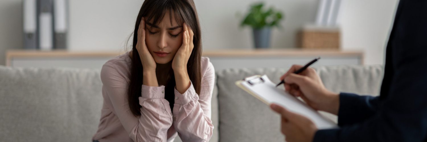 Depressed arab woman suffering from nevrous breakdown or depression, having session at psychologist's office and touching temples. Stressed patient meeting with therapist
